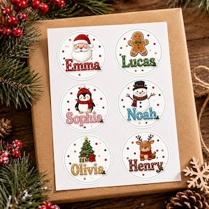 Könnte beinhalten: Ein Bogen mit sechs runden Weihnachtsaufklebern, die festliche Motive wie den Weihnachtsmann, einen Lebkuchenmann, einen Pinguin, einen Schneemann, einen Weihnachtsbaum und ein Rentier zeigen, jeweils personalisiert mit den Namen Emma, Lucas, Sophia, Noah, Olivia und Henry.
