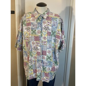 May include: A short-sleeved button-down shirt featuring a multi-colored patchwork pattern. The design includes squares with floral motifs, hearts, and geometric shapes in shades of blue, green, red, and yellow. It has a standard collar.