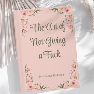 May include: A hardcover book titled "The Art of Not Giving a Fuck" by Brianna Beckman. The book has a light pink cover with floral corner accents. The title is in a cursive font.