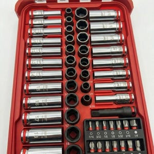 Puede incluir: Una caja de herramientas roja con tapa transparente, llena de llaves de vaso, puntas y un trinquete. Las llaves de vaso son plateadas con bandas rojas. Las medidas están en pulgadas y mm.