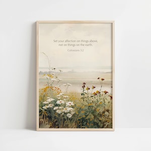 Puede incluir: Una impresión enmarcada que presenta un paisaje en acuarela con flores silvestres en primer plano. La obra de arte incluye el texto: "Poned la mira en las cosas de arriba, no en las de la tierra. Colosenses 3:2."