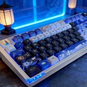 May include: A mechanical keyboard with a white and silver frame. The keycaps are a mix of black, white, and blue, with custom designs. The keyboard has a blue LED light strip along the bottom edge. The ESC keycap features a lighthouse.