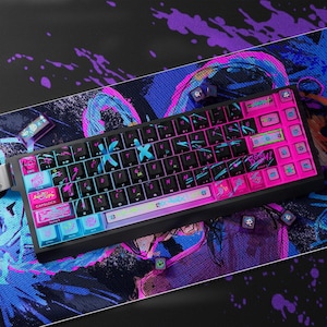 Puede incluir: Un teclado mecánico negro y rosa con teclas personalizadas. El teclado presenta una combinación de colores vibrantes con acentos rosas, azules y morados. Las teclas tienen diseños y símbolos únicos. Sobre una alfombrilla a juego.