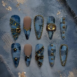 May include: A set of ten press-on nails featuring a blue denim patchwork pattern. The designs include gold metal studs, small gold stars, a miniature belt buckle detail, and a circular frame with a central star. Some nails have a matte nude base.