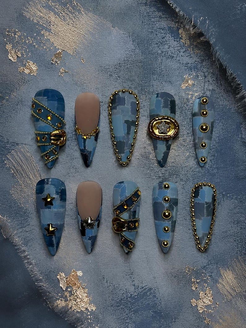 May include: A set of ten press-on nails featuring a blue denim patchwork pattern. The designs include gold metal studs, small gold stars, a miniature belt buckle detail, and a circular frame with a central star. Some nails have a matte nude base.