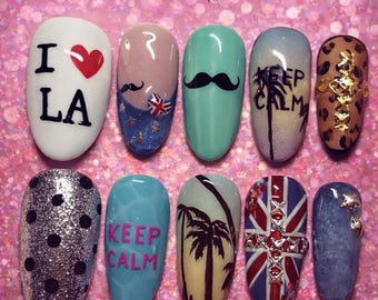 May include: A set of ten artificial nails with various designs. The designs include the text "I ❤️ LA", a mustache, a Union Jack, a palm tree, and the words "KEEP CALM". The nails are painted in various colors, including white, blue, and silver.