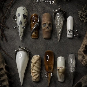 May include: A set of ten press-on nails featuring diverse designs including a skull, rib cage, tooth, and silver metal spikes. The nails vary in shape, color, and texture, with some being translucent, opaque white, or brown. The text Art Therapy is visible.