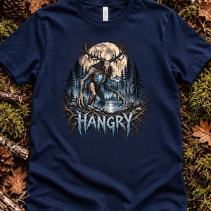 May include: A navy blue t-shirt featuring a graphic of a skeletal deer-like creature with large antlers standing in a forest before a full moon. The creature has a glowing blue heart. The word HANGRY is printed in blue below the creature.