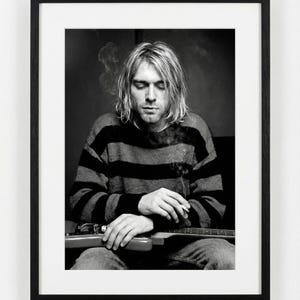 May include: Black and white framed print featuring a portrait of a person with long blonde hair, wearing a striped sweater, and holding a guitar. The person is smoking a cigarette. The image is in a black frame.