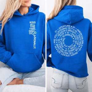 May include: A royal blue hoodie with white text on the front and back. The front reads "KISS ALL THE TIME. DISCO OCCASIONALLY." The back features a circular design with song titles and phrases. A kangaroo pocket is visible.
