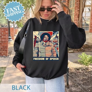 May include: Black sweatshirt featuring a graphic of a man with an afro and glasses, with the words "FREEDOM OF SPEECH" below. The graphic is in red, blue, and beige tones. The sweatshirt is worn by a person with blonde hair and sunglasses.