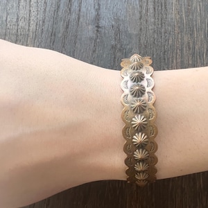 May include: A copper-toned metal cuff bracelet featuring a central row of raised, pointed conical studs. The edges of the bracelet have a scalloped design with stamped semi-circular patterns surrounding each of the nine prominent metal spikes.