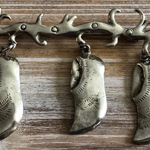 May include: Silver brooch with three dangling shoe charms. The brooch features a stylized bird design with intricate details.