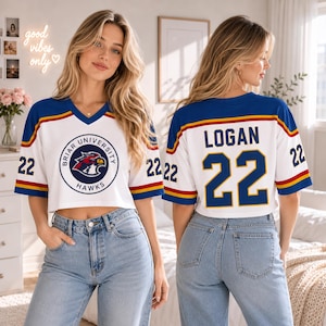 May include: White cropped jersey with blue and gold accents, featuring "Briar University Hawks" logo on the front and "LOGAN 22" on the back. The jersey has a V-neck and short sleeves, with the number "22" on both sleeves.
