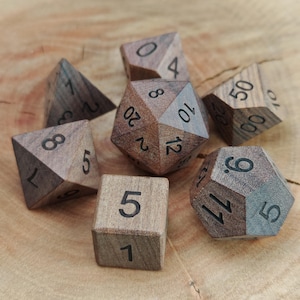 May include: A set of seven wooden polyhedral dice, each with black etched numbers. The dice are various shapes, including a cube, a d4, a d6, a d8, a d10, a d12, and a d20. The dice are arranged on a wooden surface.