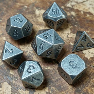 May include: A set of seven metal dice with a worn, aged appearance. The dice are in different polyhedral forms, such as a d20, d12, d10, d8, d6, and d4, each with easily seen numbers. The dice are displayed on a wooden surface.