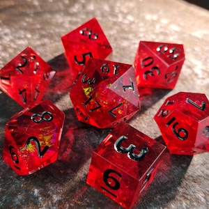 May include: Set of seven red, translucent polyhedral dice with black numbering. The dice are various shapes, including a d4, d6, d8, d10, d12, d20, and a percentile die. The dice are for tabletop role-playing games.