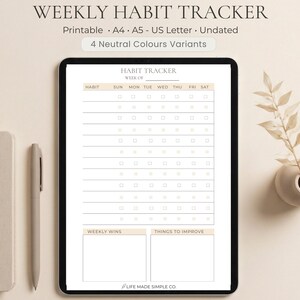 May include: A digital weekly habit tracker on a tablet, with sections for each day of the week. The tracker is undated and includes space for weekly wins and areas to improve. A pen and notebook are next to the tablet. The text on the image says "Weekly Habit Tracker".
