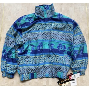 May include: A vintage blue, teal, and navy jacket with a high collar and a patterned design. The jacket features a mix of geometric shapes and floral elements. The jacket is made of pure silk.