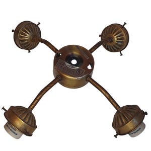 May include: A four-light ceiling fixture with an antique brass finish. The central circular mount connects to four curved, twisted arms, each ending in a fluted socket cup with small adjustment screws and a white interior light bulb base.