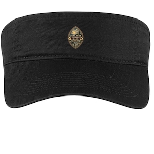 May include: A black visor featuring a centered, diamond-shaped emblem. The emblem displays a sunset over a landscape with the text GUAM and EAST COAST printed in white lettering, surrounded by a decorative border with small floral accents.