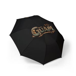 May include: Black umbrella with the word "GUAM" in a decorative, vintage-style font. The text is in shades of brown, gold, and teal, with a palm tree graphic. The umbrella is open and angled, showcasing the design.