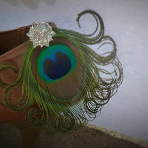 May include: A brown shoe with a peacock feather and a silver rhinestone embellishment.