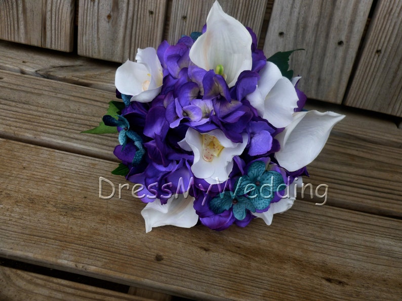 May include: A purple and white bridal bouquet with calla lilies and hydrangeas. The bouquet is accented with teal blue flowers.