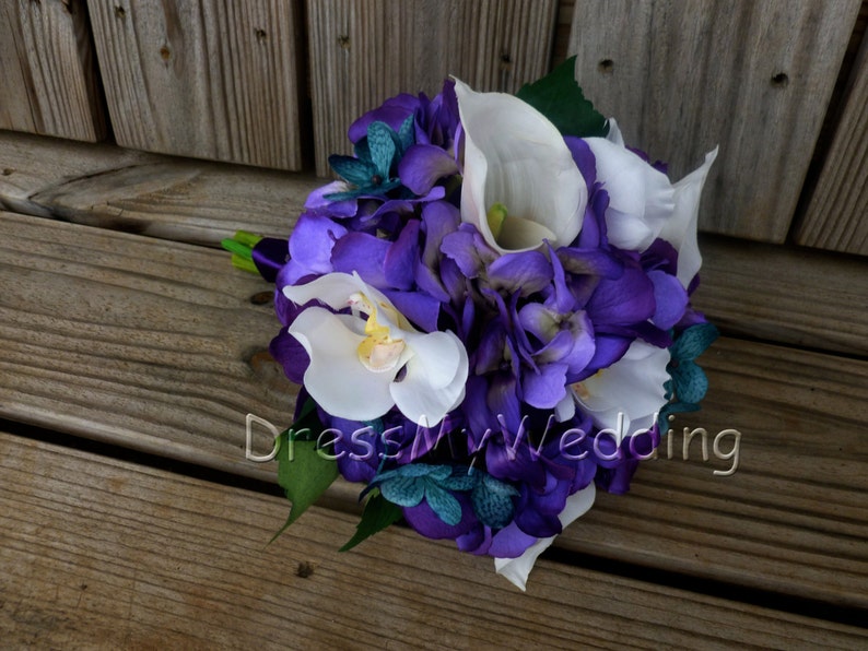 May include: A purple and white bridal bouquet with hydrangeas, calla lilies, and orchids. The bouquet is accented with teal green foliage.
