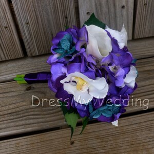 May include: A purple and white bridal bouquet with hydrangeas, orchids, and calla lilies. The bouquet is tied with a purple ribbon and has green leaves.