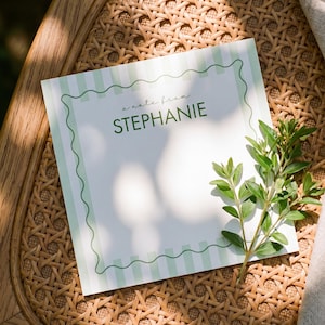 May include: A square stationery card featuring a light green and white vertical striped border with a wavy dark green line frame. The text "a note from" is printed in a script font above the name "STEPHANIE" in a bold, dark green sans-serif font.