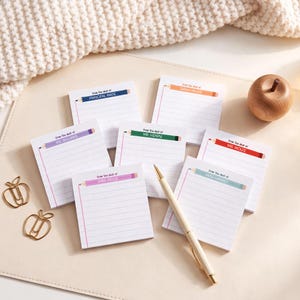 May include: A collection of seven rectangular sticky note pads with lined paper, each featuring a colorful pencil graphic at the top with the text From the desk of followed by a name. Includes two apple-shaped gold paper clips and a gold pen.