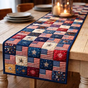 May include: A patriotic table runner with a patchwork design featuring American flags, stars, and fireworks in red, white, and blue. The runner is rectangular with a dark blue border and is placed on a wooden table.