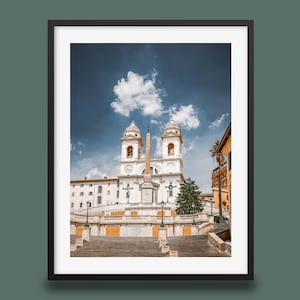 May include: Framed print of the Spanish Steps in Rome, Italy, featuring the Trinità dei Monti church. The image captures the iconic staircase, the obelisk, and the church's twin bell towers under a partly cloudy blue sky.