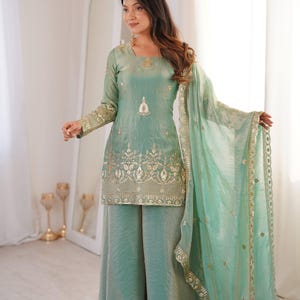 Peut inclure: Un ensemble vert d'eau composé d'un haut tunique et d'un pantalon large, orné de broderies dorées. La tenue comprend une écharpe transparente assortie avec une bordure dorée. Les manches et l'encolure de la tunique sont également ornées de détails dorés.