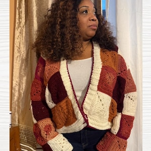 May include: A patchwork crochet cardigan in shades of cream, burgundy, and orange. The open-front sweater features a geometric pattern with square and rectangular blocks. The sleeves are long and flared, and the cardigan is worn over a white top.