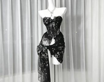 May include: A black strapless corset top and matching skirt set featuring a silver star pattern. The corset has a central black ribbon bow, while the skirt includes a long, sheer, draped side panel with a matching bow and lace trim details.