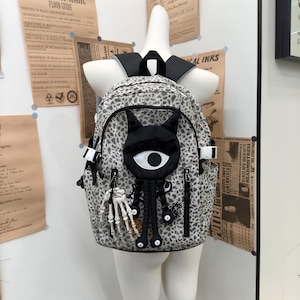 Zaino Grunge Goth grigio leopardato in nylon, decorazione horror con occhio di gatto e mano scheletrica, tracolla regolabile, grande capacità, ideale per studenti e viaggi.