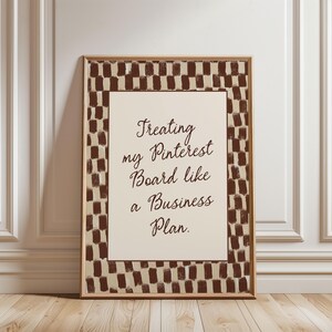 May include: A framed print with the text "Treating my Pinterest Board like a Business Plan." The print has a cream-colored background with the text in brown script. The frame has a brown and cream checkered pattern.