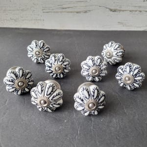 May include: Eight floral cabinet knobs. Each knob has a white base with black petal designs and a silver centre. These decorative knobs are ideal for adding a touch of elegance to furniture.