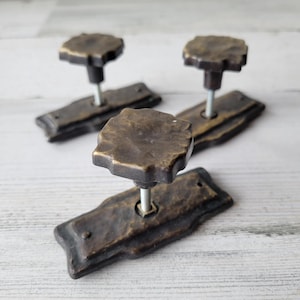 May include: Three antique bronze cabinet knobs with a textured, organic design. Each knob features a unique, irregular shape and is mounted on a rectangular backplate. The knobs are attached with a silver-colored screw.