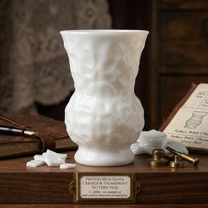May include: A white Fenton milk glass vase featuring a crinkle and thumbprint pattern. The vase has a flared rim and a pedestal base. A brass plaque on the front reads: Fenton Milk Glass, Crinkle & Thumbprint Pattern Vase, C. 1950s - An example of mid-century American pressed glass.