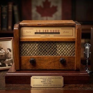 Puede incluir: Radio de válvulas Vintage Canadian General Electric, modelo CL-543-A, circa 1950. La radio de madera tiene un dial con números y una cubierta de altavoz de malla. Una foto familiar enmarcada, un micrófono y libros están cerca.
