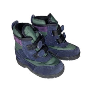 Puede incluir: Un par de botas de invierno para niños. Las botas son de color azul marino, verde y morado con correas de velcro negras. Las botas tienen una construcción de ante y nailon.