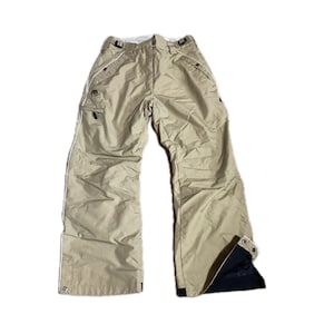May include: Beige snow trousers with white edging and several pockets. The trousers have a loose fit and feature a black interior at the leg bottoms. Designed for winter sports and outdoor activities.