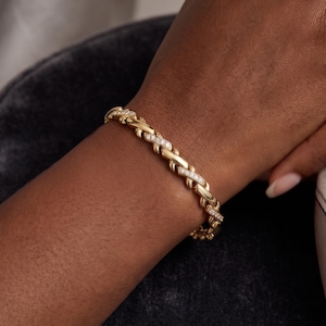 May include: A gold bracelet featuring an interlocking X-shaped link design. The bracelet is constructed with alternating polished gold links and smaller links encrusted with small, clear, sparkling stones set along the top surface of the band.