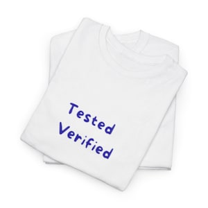 May include: Two white t-shirts are stacked. The top shirt has the words "Tested Verified" printed in blue. The shirts are folded and appear to be made of a soft material.