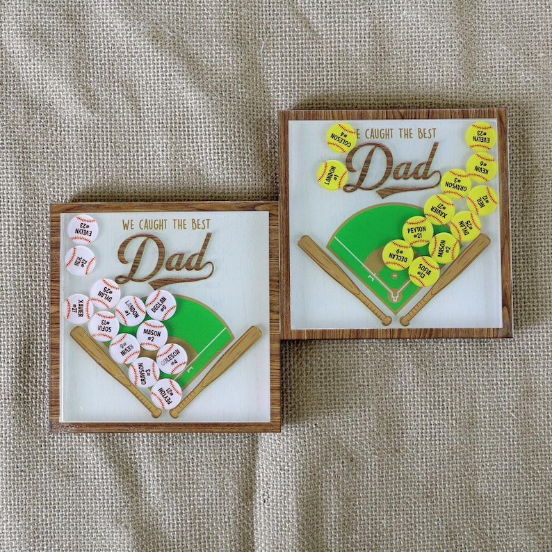 May include: Two square wooden plaques with baseball designs. Each plaque features a green baseball field, wooden bats, and baseballs with names and numbers. The text "WE CAUGHT THE BEST Dad" is displayed on one plaque, and "E CAUGHT THE BEST Dad" on the other.
