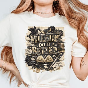 May include: Cream-colored t-shirt with a graphic design featuring the text "VILLAINS DO IT BETTER." The design includes a dragon, crown, sword, and open book illustrations. Additional text includes "obsessed," "just five minutes," "enemies to lovers," and "the villain gets the girl."