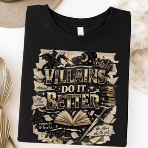 May include: Black t-shirt with a graphic design featuring the text "VILLAINS DO IT BETTER". The design includes a dragon, crown, sword, open book, and roses. Additional text includes "obesseed", "just five minutes", "enemies to lovers", and "the villian gets the girl".
